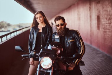 Portre çekici bir çift - vahşi motorcu siyah deri ceketli bir motosiklet ve arıyorum Genç Seksi esmer kız arkadaşına bir footway bir köprü altında oturan gözlüklü sakallı