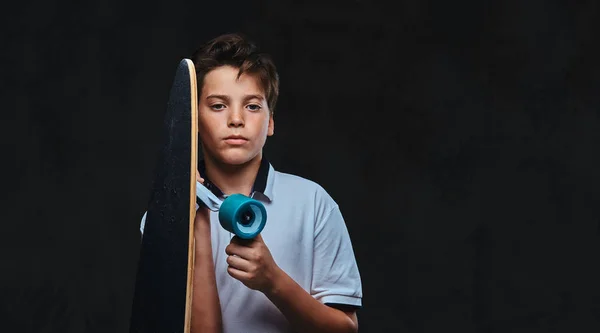 Portrait of a young skater boy dressed in a white t-shirt holds a longboard. Isolated on the dark background. — Stock Photo, Image