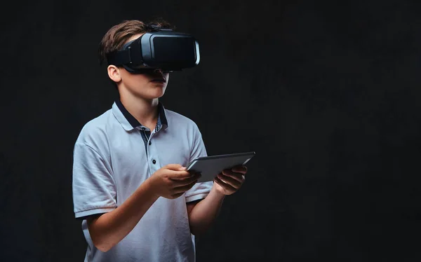 Retrato de um jovem estudante vestido com uma camiseta branca usando óculos de realidade virtual e tablet . — Fotografia de Stock