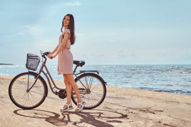 Gülümseyen sevimli kız elbise giymiş onun bisiklet ile sahilde güneşli bir günde yürür.