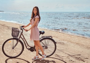 Gülümseyen sevimli kız elbise giymiş onun bisiklet ile sahilde güneşli bir günde yürür.