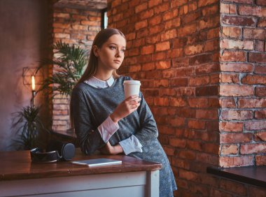 Paket servisi olan restoran kahve uzak bir oda çatı iç tablo eğilerek arayan genç kız zarif bir gri elbise giymiş tutar.