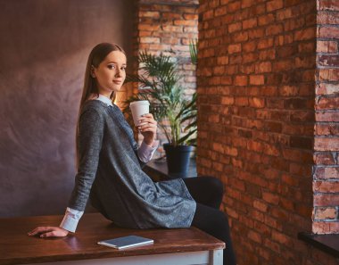 Zarif bir gri elbise giymiş genç bir kızın portresi paket servisi olan restoran kahve çatı iç ile bir odada bir masada otururken bir kameraya bakıyor tutar.