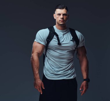 Kas yakışıklı vücut geliştirmeci spor sırt çantası gri bir arka planda poz ile.