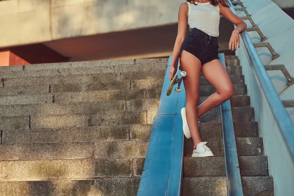 裁剪照片的一个漂亮的女孩穿着短裤和 T恤保持滑板站在台阶上 — 图库照片