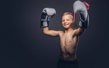 Neşeli gömleksiz çocuk boksör boks eldivenleri bir stüdyoda poz altın madalya almıştır. Karanlık bir arka plan üzerinde izole.