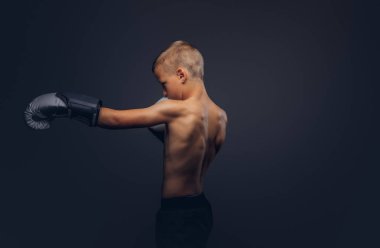 Gömleksiz çocuk boksör boks eldivenleri egzersiz bir stüdyoda giyen sarı saçlı. Karanlık bir arka plan üzerinde izole.