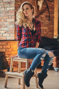 Uzun kıvırcık saçlı sarışın hippi kız büyüleyici bir polar gömlek giymiş ve kot tutan bir ahşap tabure çatı iç bir stüdyoda oturup, uzağa arıyorsunuz sabah kahve.