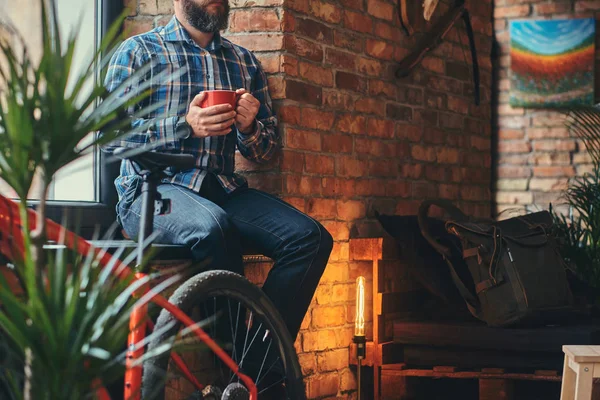 Studio loft iç pencere pervazına üzerinde otururken sabah kahve yakışıklı sakallı hippi erkek mavi Polar tişört ve kot kırpılmış görüntü tutar.