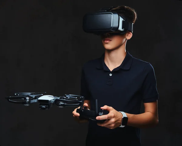 シャツに身を包んだ若いティーネー ジャーは仮想現実の眼鏡を身に着けているし リモート コントロールを使用して Quadcopter を制御します 暗い背景に分離 — ストック写真