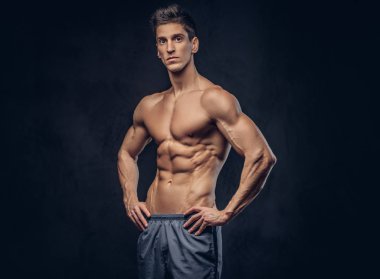 Yakışıklı gömleksiz ectomorph vücut geliştirmeci şık saç karanlık dokulu bir arka plan üzerinde poz ile.