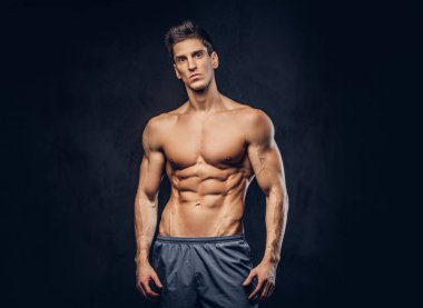Yakışıklı gömleksiz ectomorph vücut geliştirmeci şık saç karanlık dokulu bir arka plan üzerinde poz ile.