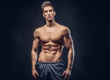 Yakışıklı gömleksiz ectomorph vücut geliştirmeci şık saç karanlık dokulu bir arka plan üzerinde poz ile.