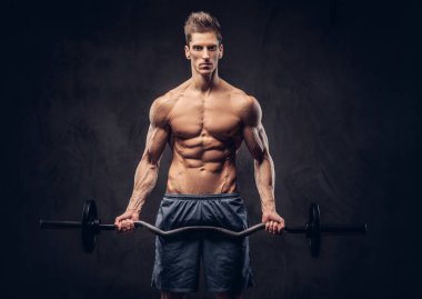 Yakışıklı gömleksiz adam şık saç ve kas ectomorph karanlık dokulu bir arka plan üzerinde halter ile egzersizleri yapıyor.