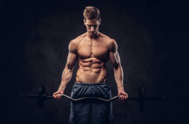 Yakışıklı gömleksiz adam şık saç ve kas ectomorph karanlık dokulu bir arka plan üzerinde halter ile egzersizleri yapıyor.