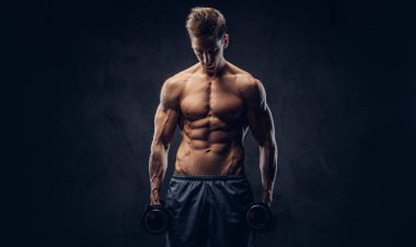 Yakışıklı gömleksiz adam şık saç ve kas ectomorph vücut egzersizleri karanlık dokulu bir arka plan üzerinde dumbbells ile yapıyor.
