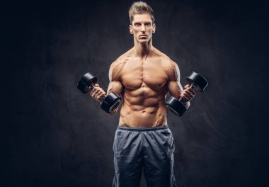 Yakışıklı gömleksiz adam şık saç ve kas ectomorph vücut egzersizleri karanlık dokulu bir arka plan üzerinde dumbbells ile yapıyor.