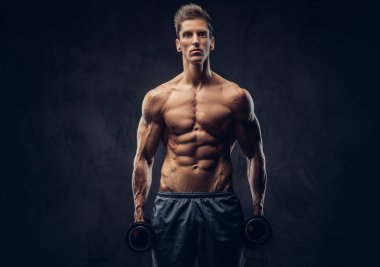 Yakışıklı gömleksiz adam şık saç ve kas ectomorph vücut egzersizleri karanlık dokulu bir arka plan üzerinde dumbbells ile yapıyor.