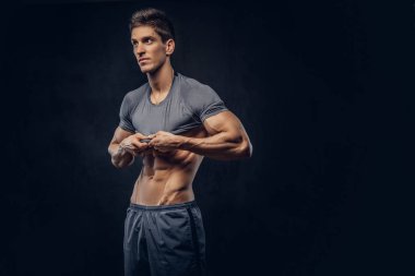 Gömleğini karanlık bir arka plan üzerinde kapalı şık ectomorph vücut geliştirmeci şık saç ile alır.