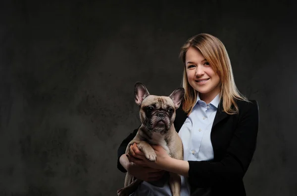 Portrait of a smiling blonde woman breeder holds her cute pug. Isolated on dark textured background. — Stock Photo, Image