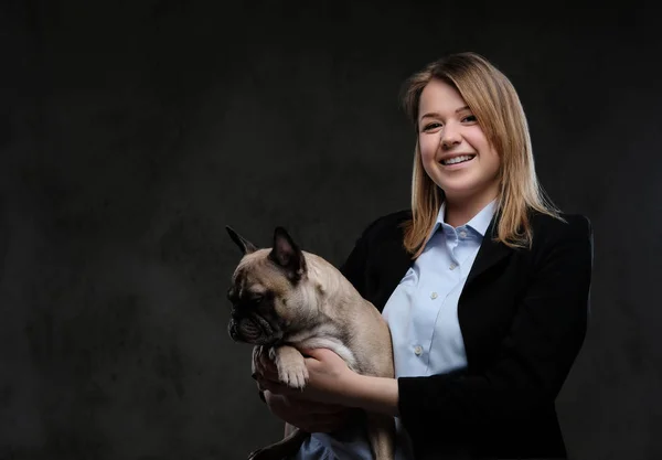 Portrait of a smiling blonde woman breeder holds her cute pug. Isolated on dark textured background. — Stock Photo, Image