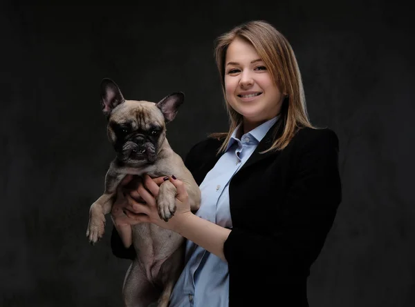 Portrait of a smiling blonde woman breeder holds her cute pug. Isolated on dark textured background. — Stock Photo, Image