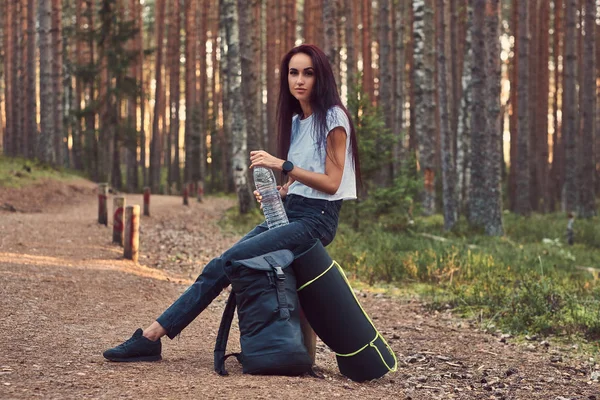 Turista chica hipster sostiene una botella de agua, se detuvo a descansar en un hermoso bosque de otoño . — Foto de Stock