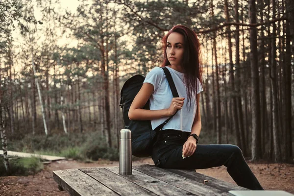 Günbatımında kırmak bir sonbahar ormanda sahip ahşap bir masa üzerinde oturan şehvetli turist kız. — Stok fotoğraf