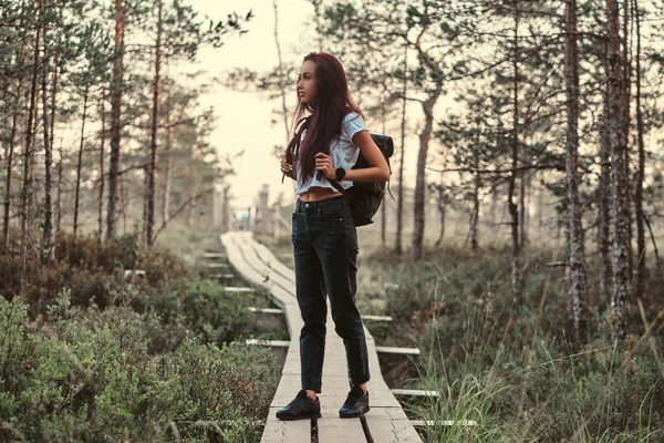 Ganzkörperporträt eines Touristenmädchens, das auf einem Holzweg in einem schönen Wald steht. — Stockfoto
