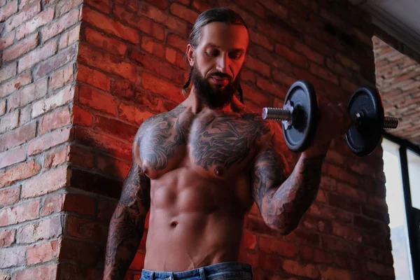 Brutal barbudo tatuado masculino fazendo exercício com um haltere em um quarto com loft interior . — Fotografia de Stock