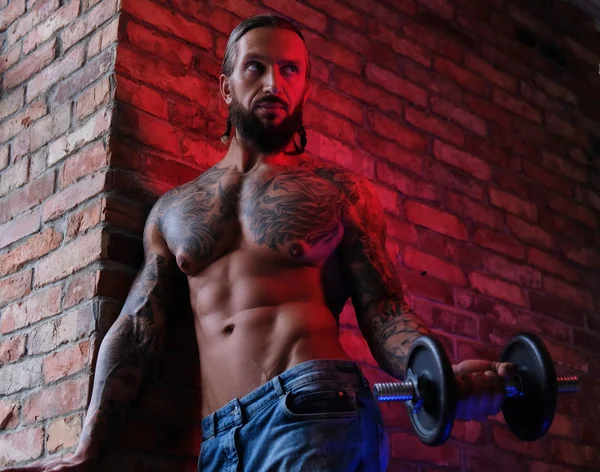 Brutal bebaarde tattooed man doen oefening met een halter in een kamer met loft interieur. — Stockfoto