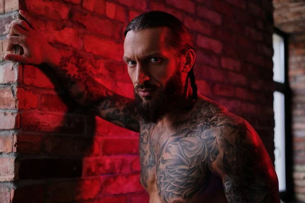 Brutale barbuto tatuato maschio posa contro muro di mattoni . — Foto Stock