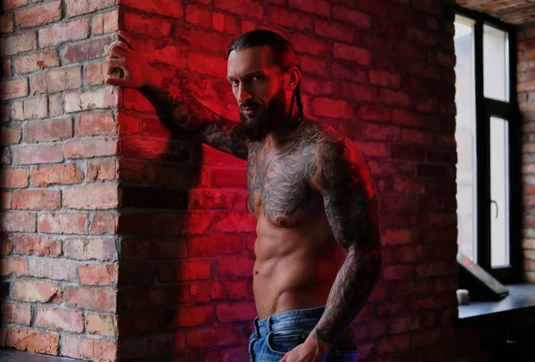Brutal bearded tattooed male posing against brick wall.