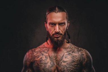 Yakın çekim fotoğraf bir acımasız gömleksiz dövmeli erkek sakallı. Karanlık dokulu bir arka plan üzerinde izole.