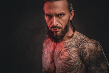 Yakın çekim fotoğraf bir acımasız gömleksiz dövmeli erkek sakallı. Karanlık dokulu bir arka plan üzerinde izole.