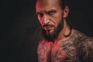 Yakın çekim fotoğraf bir acımasız gömleksiz dövmeli erkek sakallı. Karanlık dokulu bir arka plan üzerinde izole.