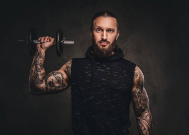 Bir halterle el poz bir siyah hoodie sakallı dövmeli atlet portresi.