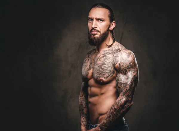 Egy félmeztelen, szakállas, tetovált férfi portréja. Sötét textúrázott háttérre elszigetelt. — Stock Fotó