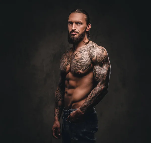 Retrato de un hombre sin camisa con barba tatuado posando con la mano en el bolsillo. Aislado sobre fondo de textura oscura . —  Fotos de Stock