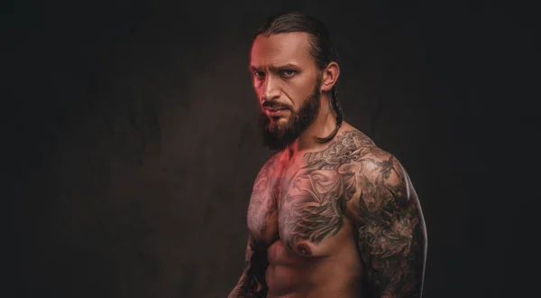Foto ravvicinata di un brutale maschio barbuto tatuato senza maglietta. Isolato su uno sfondo scuro strutturato . — Foto Stock