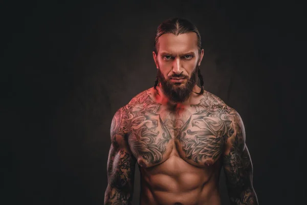 Крупный план жестокого бородатого татуированного мужчины без рубашки. Изолированный на темном текстурированном фоне . — стоковое фото