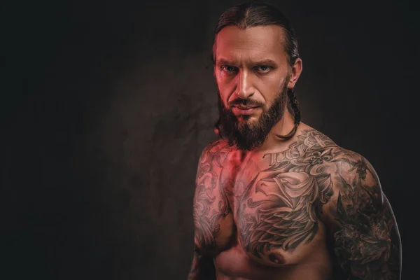 Foto de close-up de um brutal homem tatuado sem camisa de barba. Isolado em um fundo texturizado escuro . — Fotografia de Stock