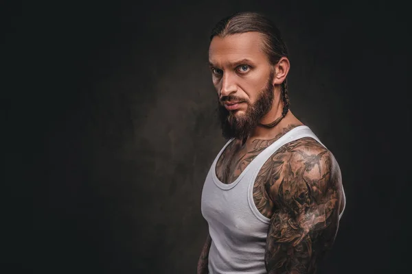 Brutal bebaarde tattooed man in een wit overhemd. Geïsoleerd op donkere gestructureerde achtergrond. — Stockfoto