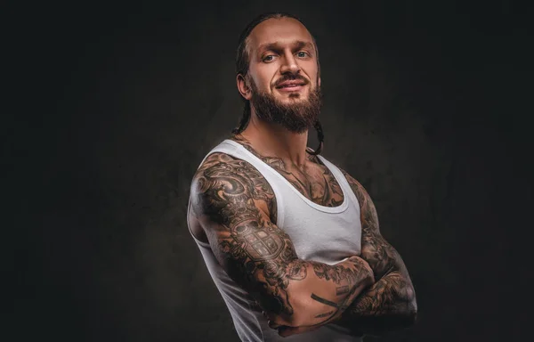 Brutal barbudo tatuado macho em camisa branca posando com os braços cruzados. Isolado em um fundo texturizado escuro . — Fotografia de Stock