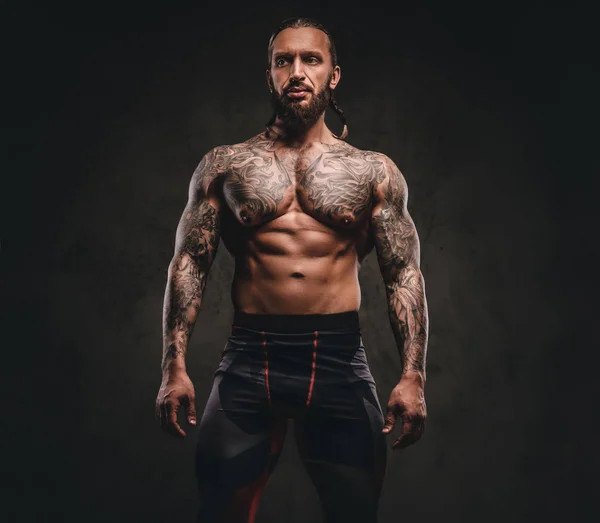 Atleta tatuado sem camisa barbudo em sportswear. Isolado em um fundo texturizado escuro . — Fotografia de Stock