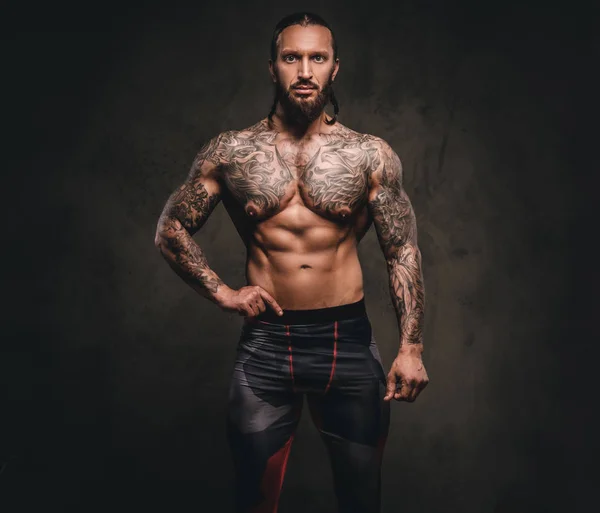 Γενειοφόρος shirtless τατουάζ αθλητής σε αθλητικά ενδύματα. Απομονωμένη σε ένα σκοτεινό φόντο με υφή. — Φωτογραφία Αρχείου