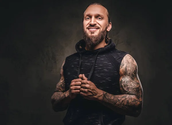 Retrato de um atleta tatuado barbudo com capuz preto. Isolado em um fundo texturizado escuro . — Fotografia de Stock