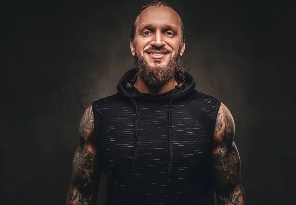 Retrato de un atleta tatuado barbudo con capucha negra. Aislado sobre un fondo de textura oscura . — Foto de Stock