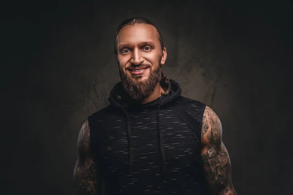 Retrato de um atleta tatuado barbudo com capuz preto. Isolado em um fundo texturizado escuro . — Fotografia de Stock