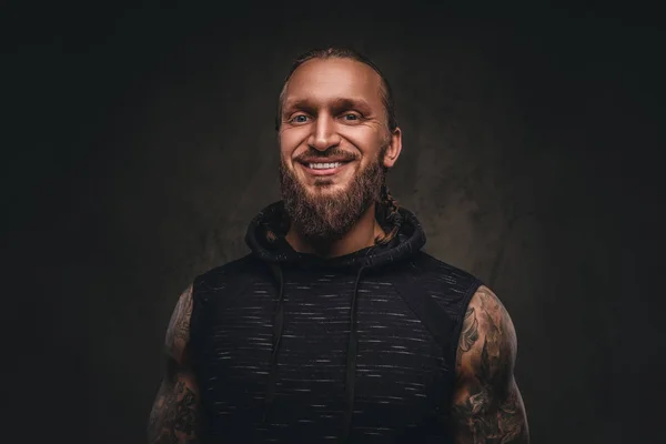 Retrato de um atleta tatuado barbudo com capuz preto. Isolado em um fundo texturizado escuro . — Fotografia de Stock